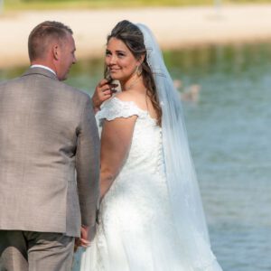 Bruid Gladys kijkt lachend over haar schouder naar bruidegom Pim tijdens hun bruidsreportage aan het water in Ewijk.