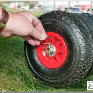Close-up van een hand die een borgpen in een rode velg van een Reich caravan rangeerhulp (mover) wiel steekt, met de banden op het gras.