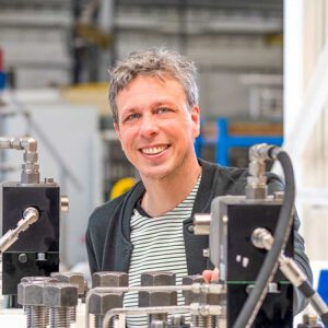 Man glimlacht tussen industriële machines in een fabriekshal – bedrijfsportret door Fotografie Arthur van Leeuwen.