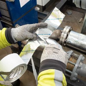 Industriële werker brengt reflecterende isolatietape (ROCKWOOL) aan om een naad op industriële leidingen af te dichten.