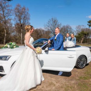Bruid kijk naar bruidegom die bij de auto staat. Kinderen op de achterbank