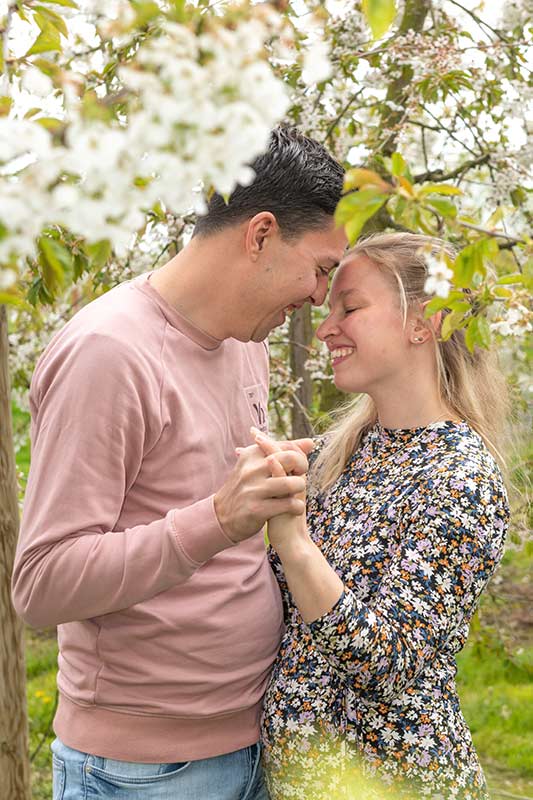 Loveshoot: verliefd stel houdt elkaars hand vast in bloeiende boomgaard
