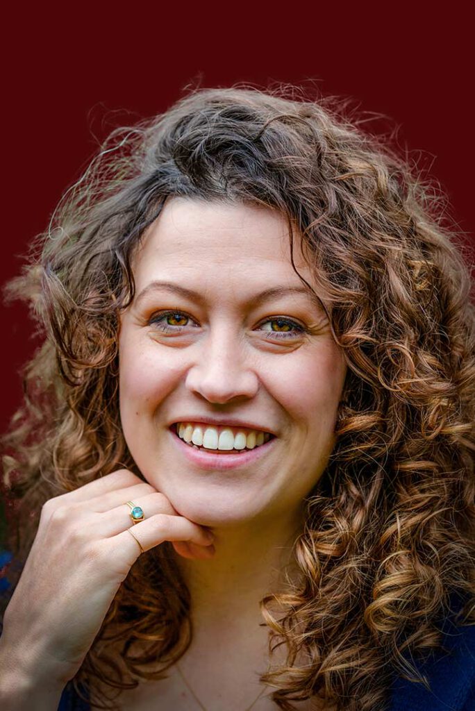 Lachend close-up portret van een vrouw met krullend haar en heterochromie voor een rode achtergrond.