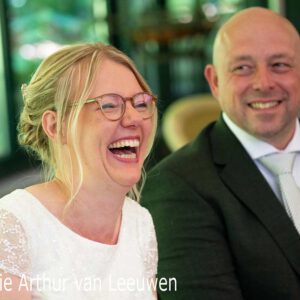 Lachende bruid met bril en glimlachende bruidegom in pak met witte stropdas, close-up.