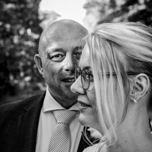 Zwart-wit close-up van bruidspaar, man kijkt naar camera, vrouw met bril kijkt opzij