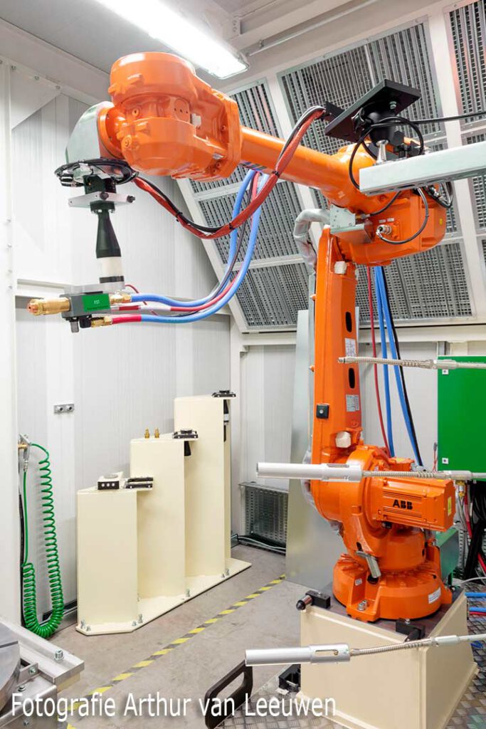 Bedrijfsfoto van een oranje industriële ABB robotarm in een fabriekshal.