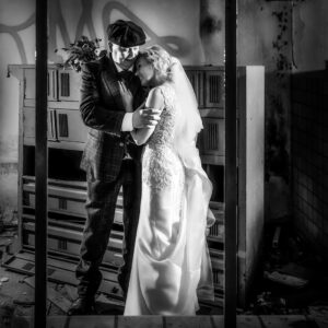Zwart-wit trouwfoto van een bruidspaar in vintage stijl, poserend in een verlaten industrieel pand met graffiti en oude lockers.
