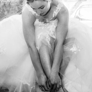 Zwart-wit foto van een bruid die haar trouwschoenen aantrekt, met focus op haar kanten bruidsjurk en een verfijnd haarsieraad.